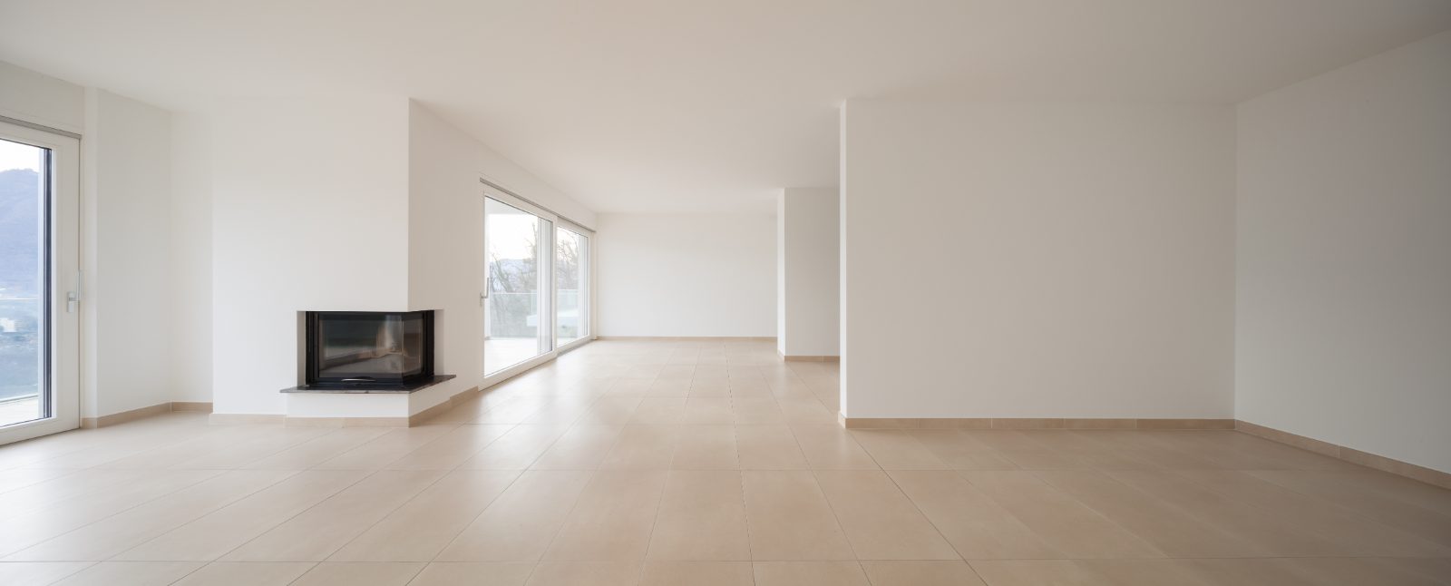 Spacious modern living room with light tile flooring, fireplace, and large windows overlooking outdoor landscape