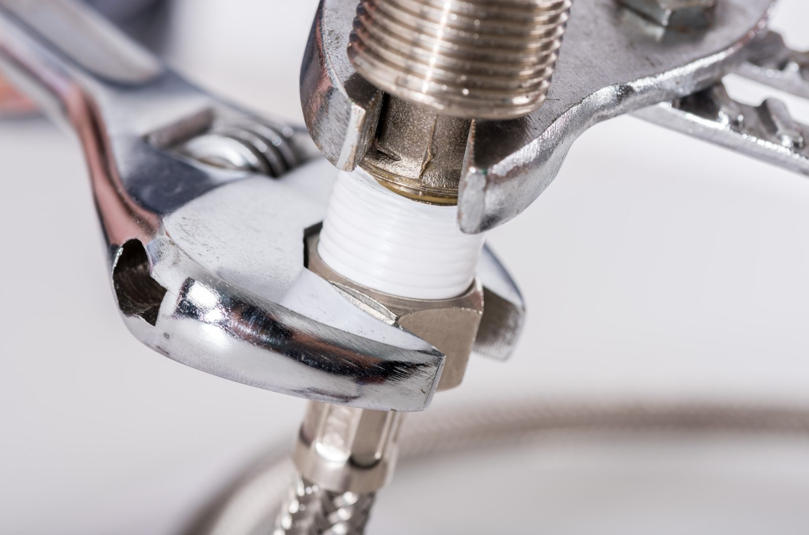 Plumber's wrench tightening a chrome faucet valve with white ferrule